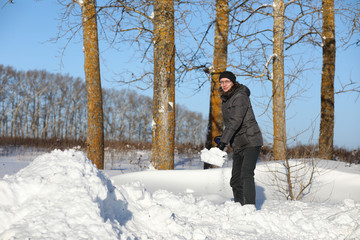 Naklejka premium man remove snow with shovel from the road in winter