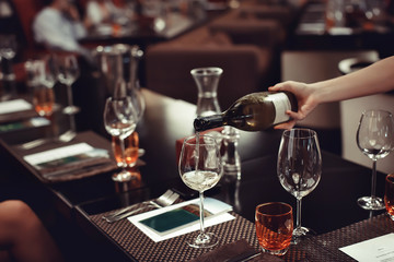 Waiter pouring wine to the glass onthe table