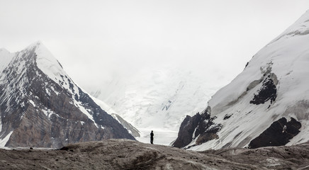 Small alone man between big mountains on glacier