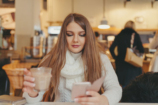 beautiful girl drinking coffee and texting on smart phone in cafe