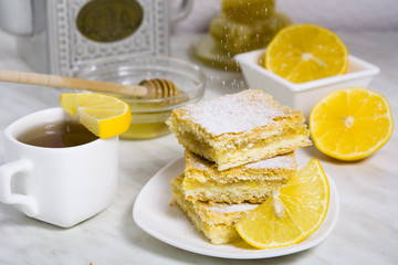 Three pieces of lemon pie with fresh lemon and cup of tea and teapot on the background