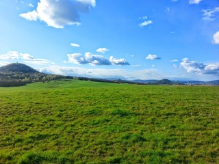 The blooming meadow with nice blue sky with dispersed clouds by sunny day. The Czech nature. Hills in the background.