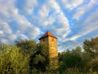 The historical tower hidden among the trees. Nice sunny day with blue sky with some clouds.