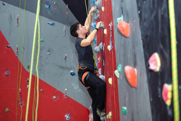 Young man climbing indoor wall and reaching the top