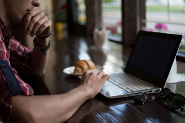 Young man freelancer working from a cafe with a laptop, hipster guy using modern laptop computer while working in a vintage loft, close-up of male hands.