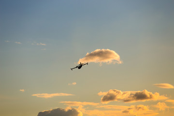 Canadair aircraft silhouette flyes in the sky through the clouds at sunset