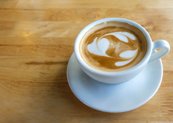 A cup of coffee with heart pattern in a white cup on wooden table background