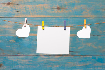 White hearts hanging over blue wooden background with blank pape