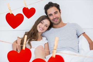 Smiling couple in bed with red heart shapes in foreground