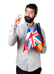 Handsome man with beard holding many flags and making tiny sign