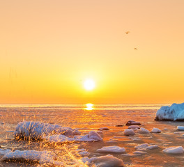 sunrise on the bank of the winter sea. The ice floes floating in the water, frozen water, the sun rising over the horizon.
