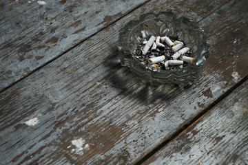 Cigarette butts in an ashtray on old wooden background.Copy space.