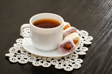 Mug of tea and Turkish delight with nuts on a plate, close-up, black background