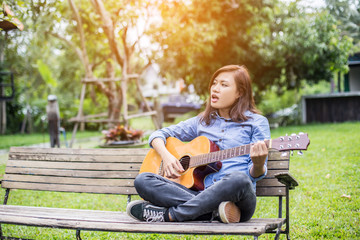 Obraz premium Beautiful young woman playing guitar sitting on bench, Happy tim