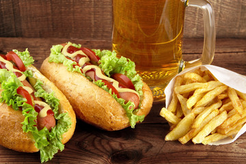 Hot dogs with glass of beer with french fries on wooden board