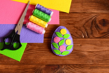 Felt Easter egg decor, scissors, thread group, needle, colored felt sheets on wooden background with copy space. Embellished felt Easter egg decorating idea. Simple and beautiful Easter gift. Top view