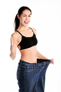 Slim woman wearing old big jeans, showing successful result of a diet – weight loss, slimming concept. White background
