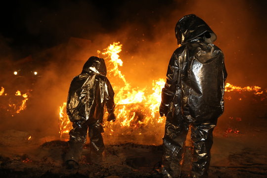 Feuerwehrmänner in Schutzkleidung lösen brennende Teile aus einem Brandherd heraus damit das Feuer besser gelöscht werden kann