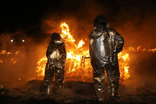 Feuerwehrmänner in Schutzkleidung lösen brennende Teile aus einem Brandherd heraus damit das Feuer besser gelöscht werden kann