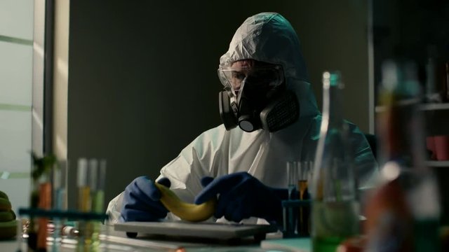 Sinister looking male scientist in bio technology laboratory holds a banana in his hands. Biological engineer research modificated additives for fruits and vegetables in food-processing industry