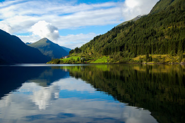 gudvangen fjord in norway refleting on the water on a blue sky with clouds background