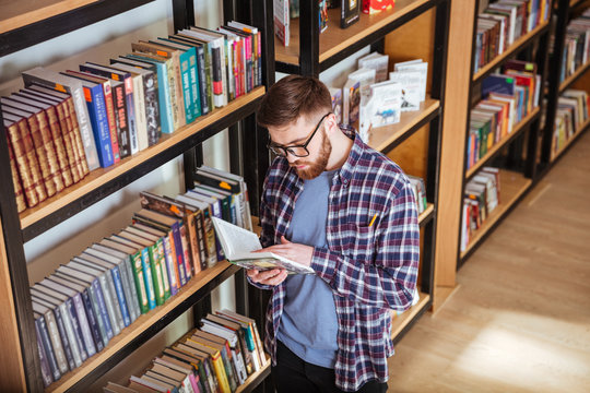 Man in glasses standing and reading in library