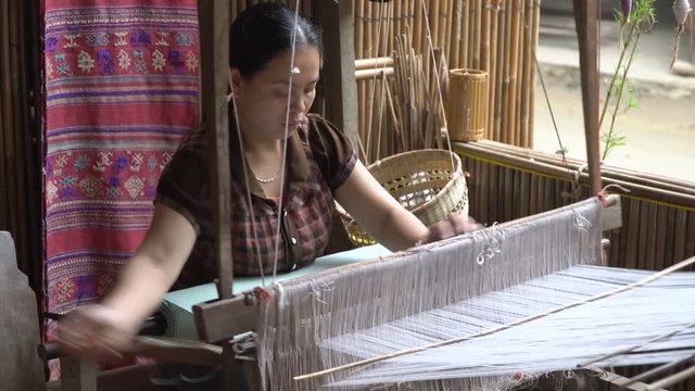 Woman working with a waist loom to finish an handcraft to sell in the market. Traditional asian textile manufacture in craft village where women work on wooden weaving loom machines