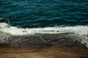 Beautiful aquamarine sea waves crash against brown stones