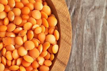Raw uncooked red lentils in wooden bowl on rustic background. Top view with copy space