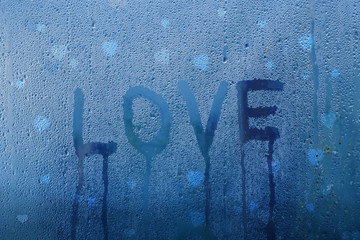 Love word handwritten on wet droplet window pane with blue light background. Selective focus used.