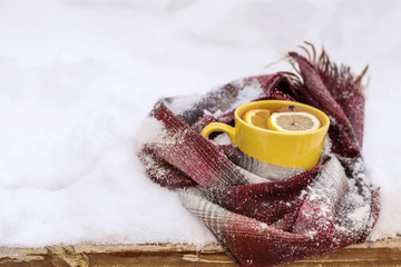  cup of of tea with lemon slice wrapped in a knitted scarf on the snow