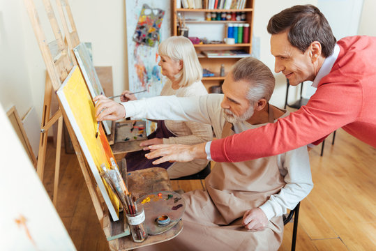Overjoyed artist helping elderly man in painting studio