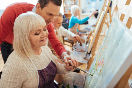 Glad man helping elderly woman in painting studio