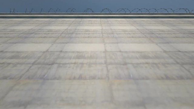 A pan across a  massively high concrete security wall topped with barbed wire over a days time lapse sky background