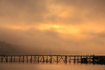 Fototapeta premium Wooden bridge across gold river with foggy background located at kanchanaburi province thailand