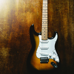 Vintage sunburst color guitar with old wood surface in background.