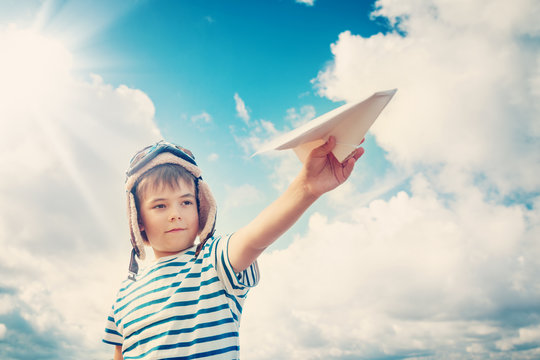 boy playing with a paper plane in aviator hat. Child outdoors in summer