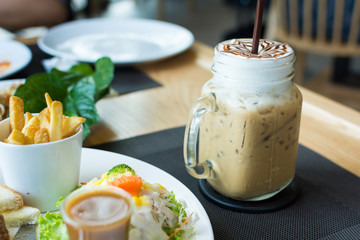 A glass of ice cappuccino art with foods on table