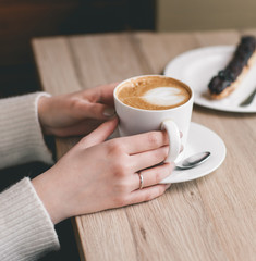 Womans hands wrapped around a cup on wood table with chocolate e