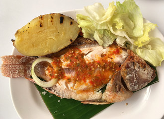 Grilled cooking red tilapia fish with spicy sauce and vegetables on the banana leaf.