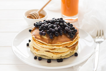 Stack of pancakes with frozen blueberries and honey on white wooden table. Selective focus
