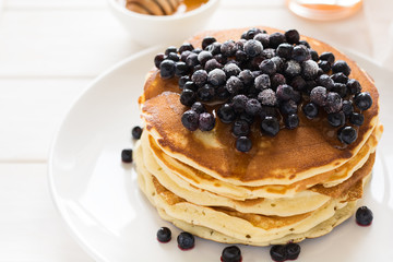 Stack of pancakes with frozen blueberries and honey on white wooden table. Selective focus