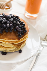 Stack of pancakes with frozen blueberries and honey on white wooden table. Selective focus