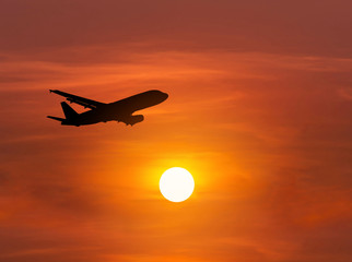             Silhouette passenger airplane flying away in to sky high altitude above the sun during sunset