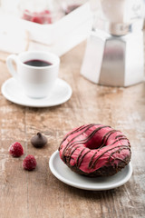 Chocolate donut/doughnut with raspberry glaze.Coffee pot and a coffee cup in the background. 