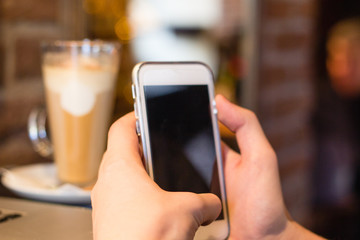 Taking picture of latte coffee with smartphone in cafe