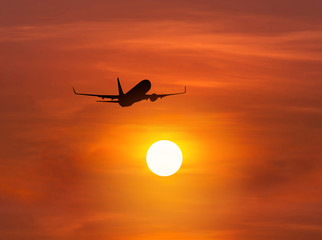 Silhouette passenger airplane flying away in to sky high altitude above the sun during sunset