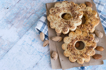  Almonds and ring cookies.    Almonds and ring cookies, strewed with chopped nuts, on paper and on a checkered napkin on an old wooden table.
