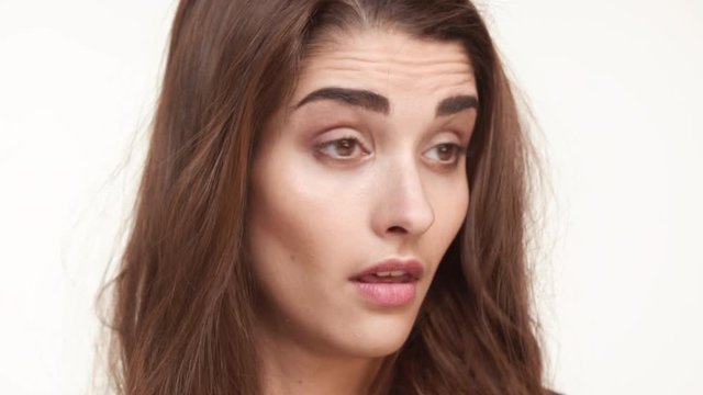 Close up footage of skeptical beautiful Caucasian female standing on white background looking forward with disappointment