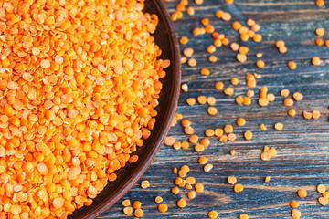Red lentils in ceramic bowl on wooden table. Selective focus. Top view.